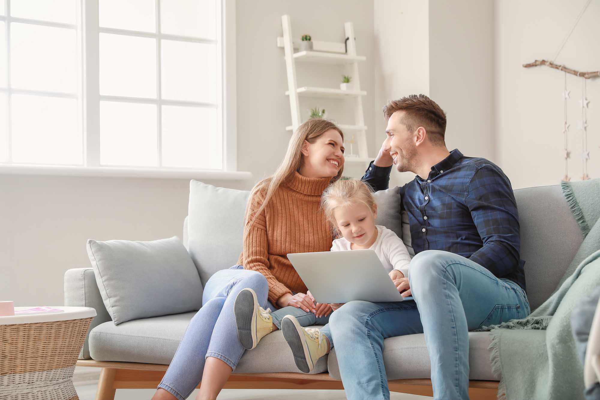 Happy young family with laptop sitting on sofa at home